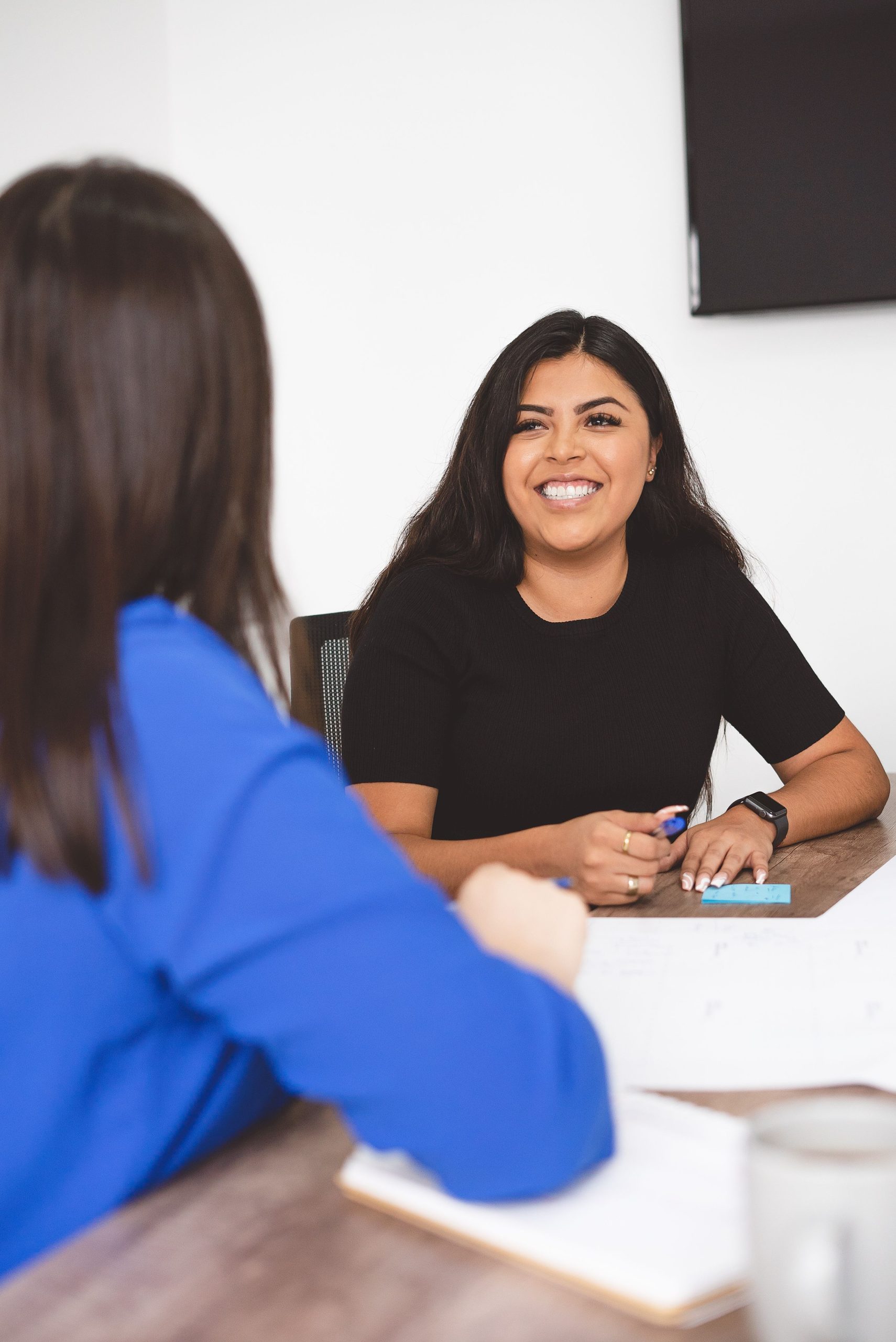Two women engaging in a business meeting, smiling confidently at each other in an office setting.